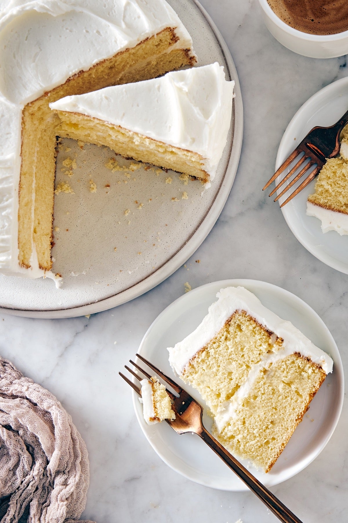 Slice of yellow layer cake with white frosting on a plate, remainder of cake on the side.er of