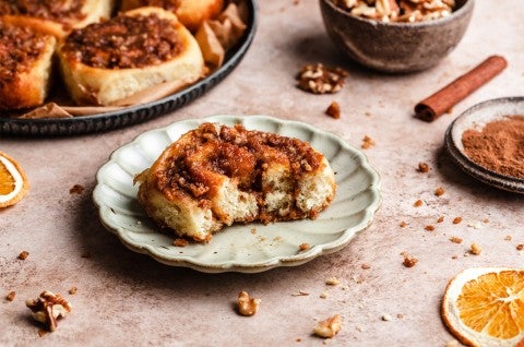 An orange sticky roll on a plate with a bite taken out of it. - select to zoom