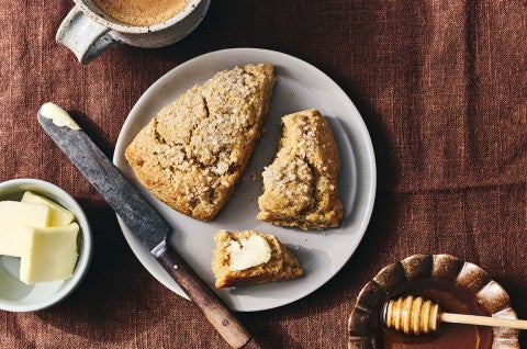 Two Golden Wheat Scones on a plate, one unbroken, the other broken with a dollop of butter on it. - select to zoom