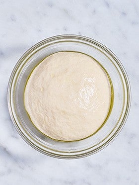 Flatbread dough in a clear bowl after rising.