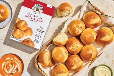 Soft Golden Buns & Rolls in a basket on a table with a box of King Arthur Baking Soft Golden Buns & Rolls mix